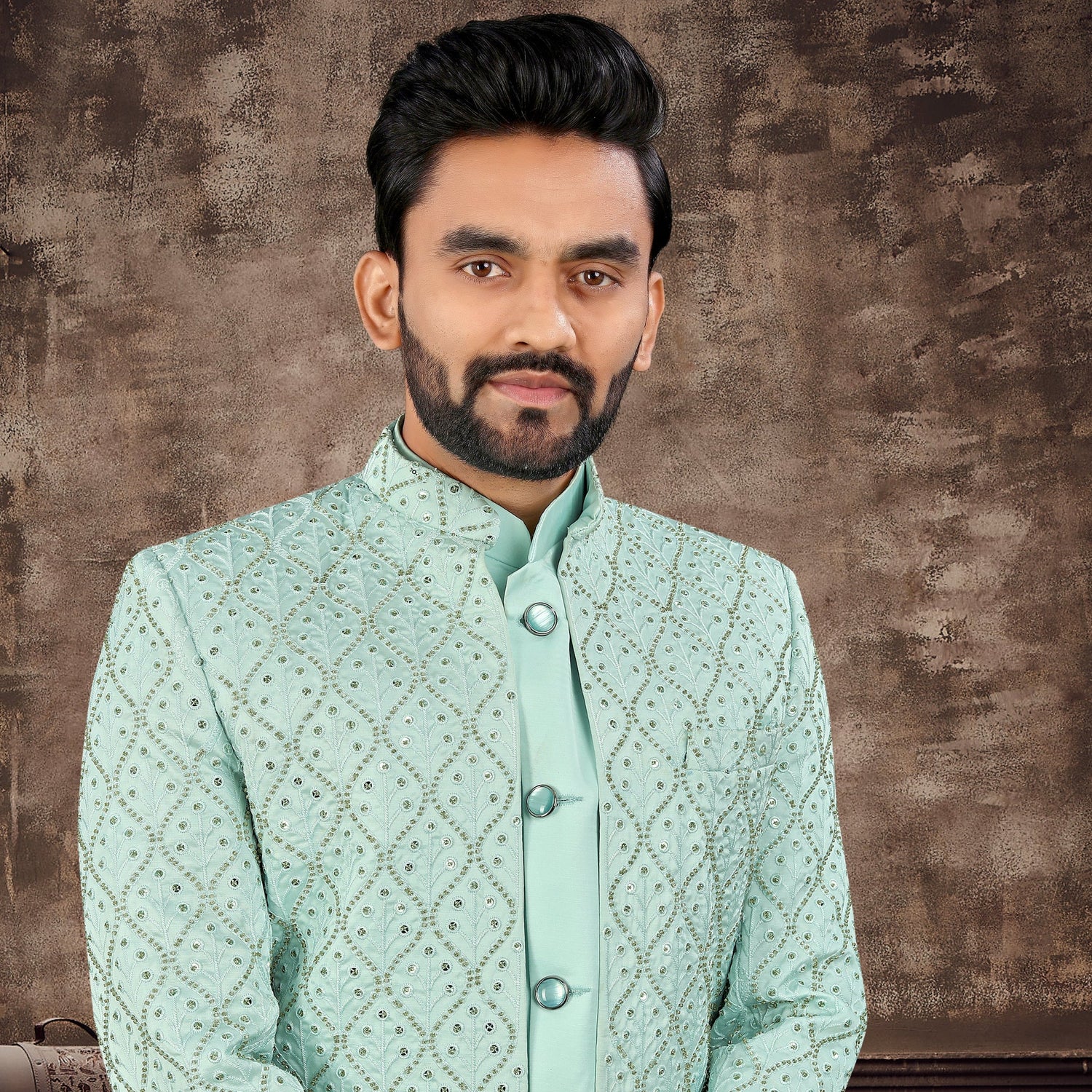 Man wearing a light green traditional outfit against a textured brown background