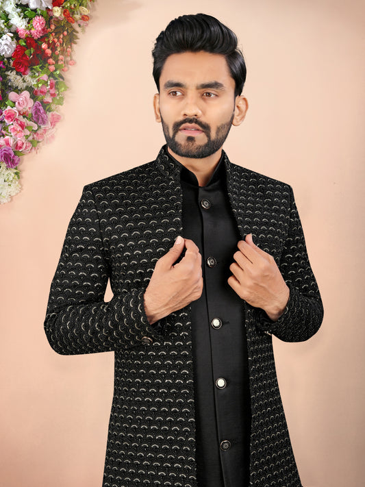 Man wearing a black patterned jacket against a beige background with floral decorations.