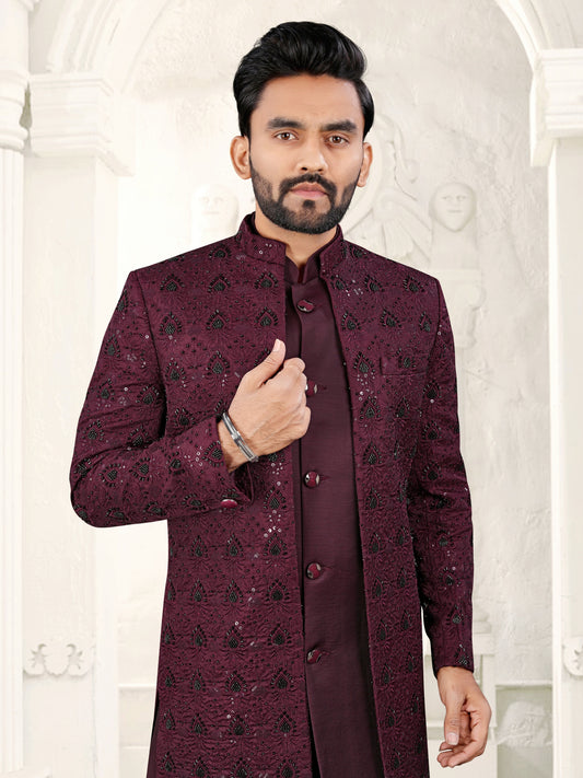 Man wearing a maroon sherwani with intricate patterns against a white background