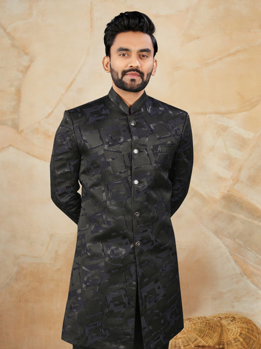 Man wearing a black patterned kurta against a beige background