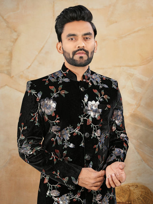 Man wearing a black floral embroidered shirt against a beige textured background