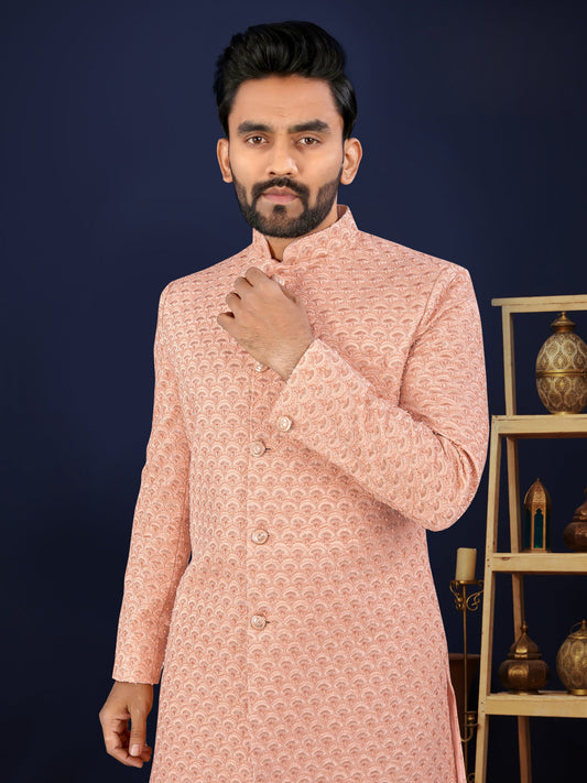 Man wearing a pink traditional sherwani against a dark background