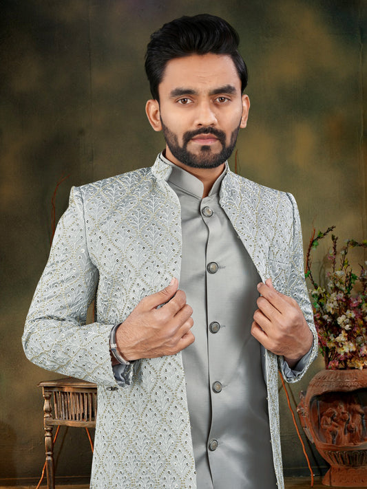 Man wearing a light gray traditional sherwani with intricate patterns, standing against a blurred background.