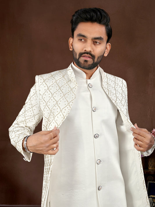 Man wearing a white embroidered sherwani against a brown background