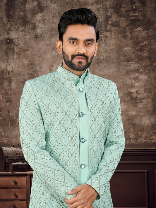 Man wearing a light green traditional outfit against a brown textured wall.