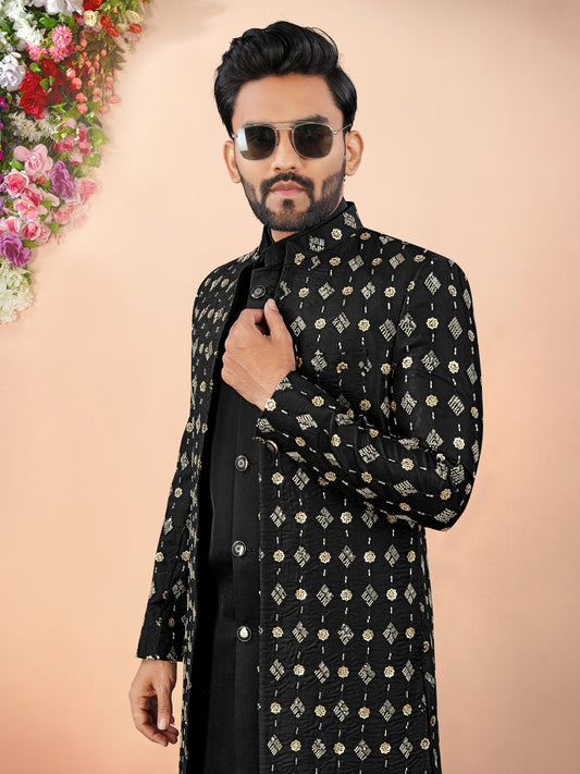 Man wearing a black embroidered sherwani with sunglasses against a beige background