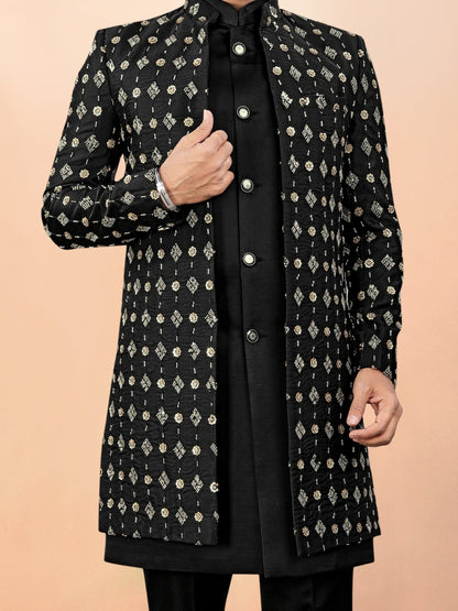 Man wearing a black and white patterned sherwani with a plain background