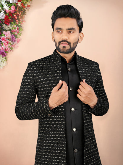 Man wearing a black patterned jacket against a beige background with floral decorations.