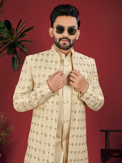 Man wearing a cream-colored sherwani with intricate patterns against a red background