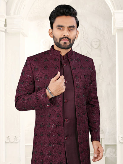 Man wearing a maroon sherwani with intricate patterns against a white background