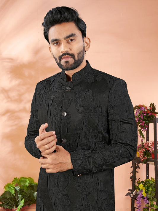 Man wearing a black traditional outfit with a decorative background