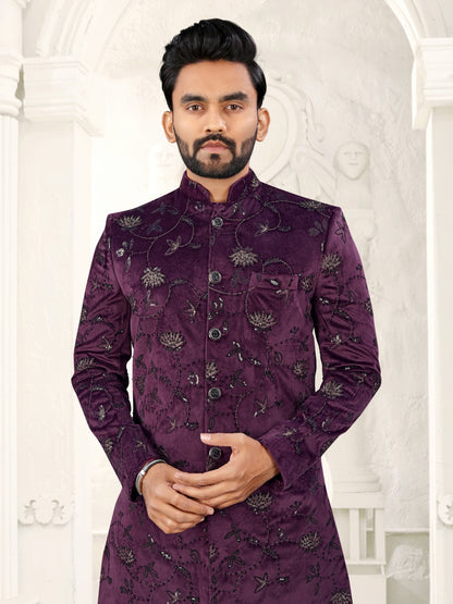 Man wearing a purple embroidered sherwani against a white decorative wall.