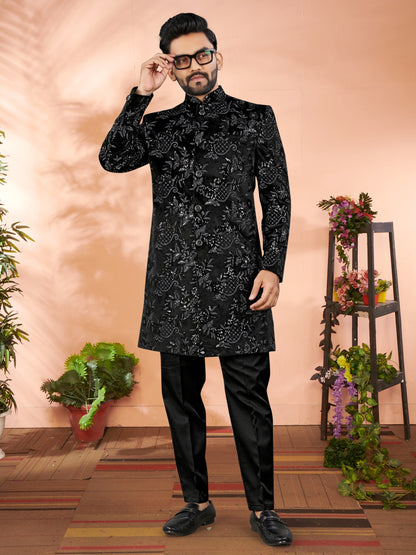 Man wearing a black embroidered sherwani with floral decorations in the background