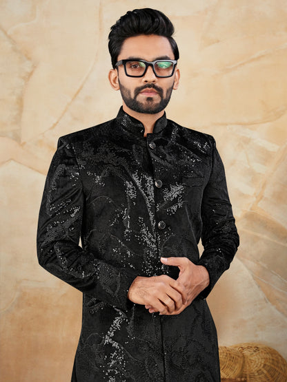 Man wearing a black embroidered traditional outfit against a beige background