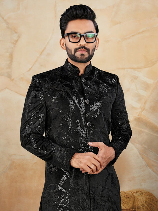 Man wearing a black embroidered traditional outfit against a beige background