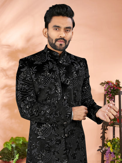 Man wearing a black embroidered traditional outfit against a pink background