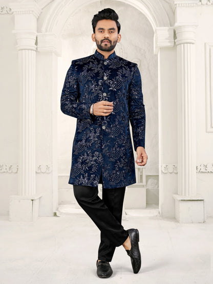 Man wearing a dark blue patterned coat with black pants in a white architectural setting