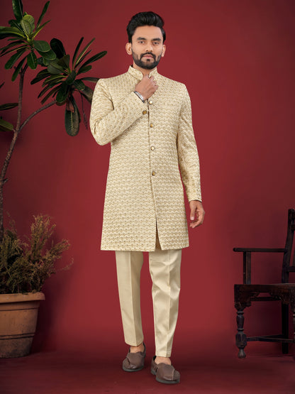 Man wearing a traditional cream sherwani against a red background