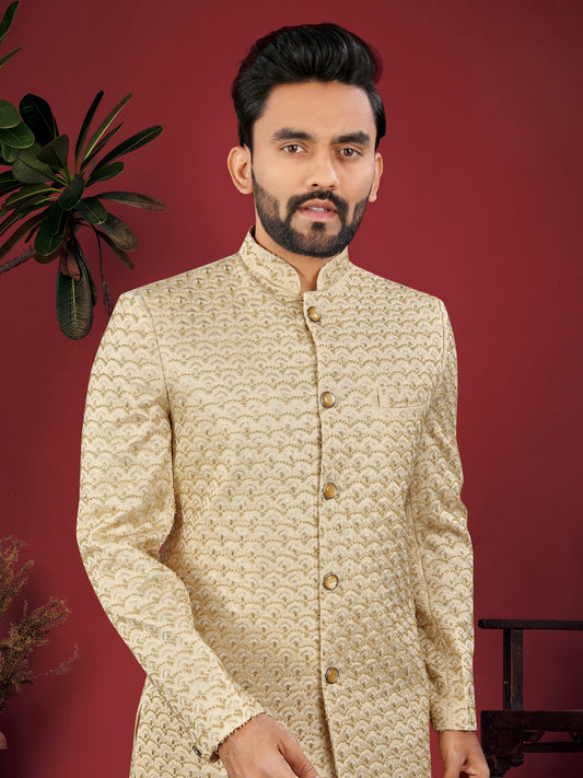Man wearing a cream patterned sherwani against a red background