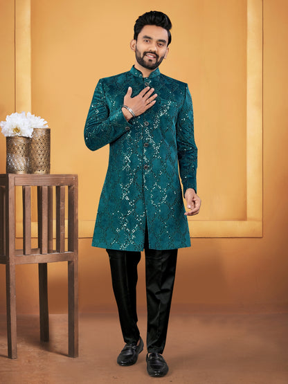Man wearing a green sherwani with black pants against an orange background