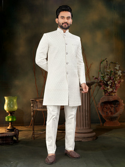 Man wearing a white traditional outfit in a decorative setting with flowers and a lamp.