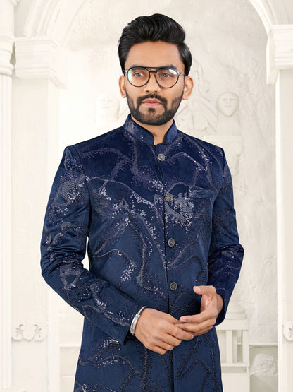 Man wearing a blue embroidered sherwani against a white decorative wall