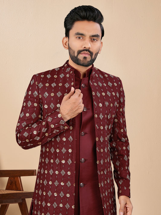 Man wearing a maroon embroidered sherwani against a beige background