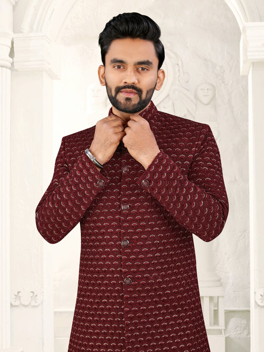 Man wearing a patterned maroon kurta against a white decorative wall