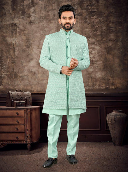 Man wearing a light green traditional outfit against a textured brown wall.
