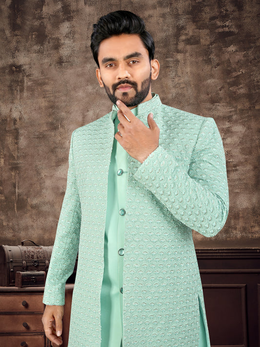 Man wearing a light green traditional sherwani against a brown textured background