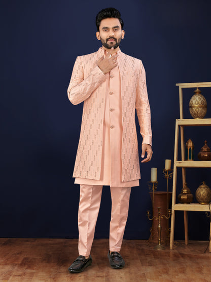 Man wearing a light pink sherwani with intricate patterns against a dark blue background.