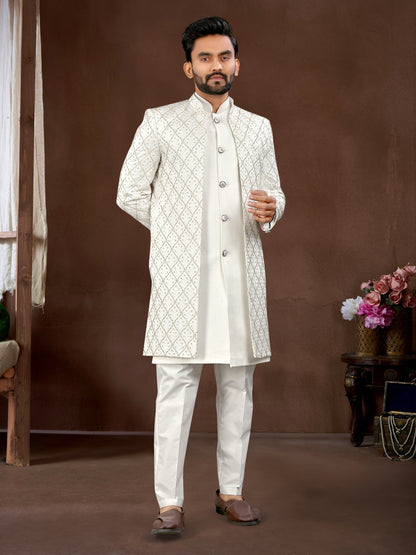 Man wearing a white sherwani with intricate patterns against a brown background