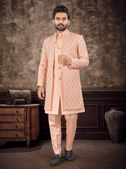 Man wearing a peach sherwani with intricate patterns in a rustic setting.