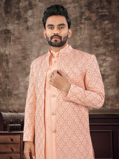 Man wearing a peach embroidered sherwani against a textured brown background