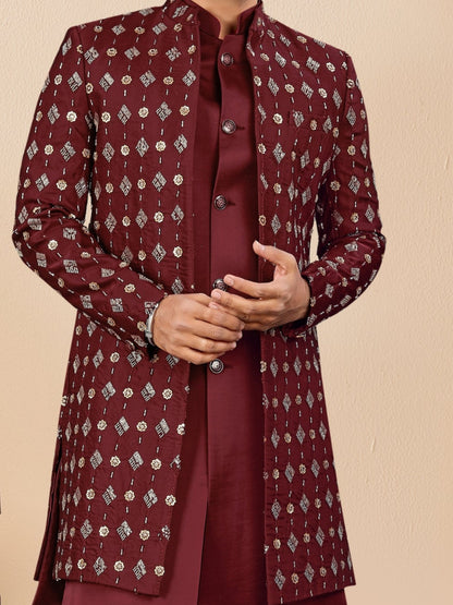Man wearing a maroon traditional outfit with a beige background