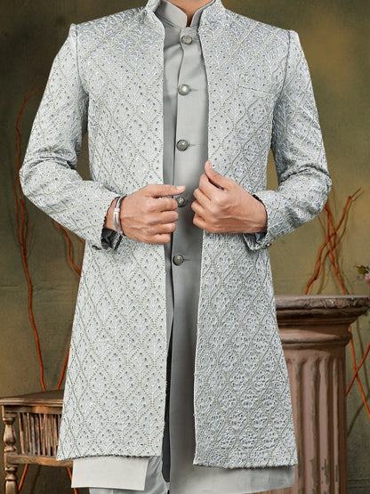Man wearing a traditional gray sherwani in a decorated indoor setting.
