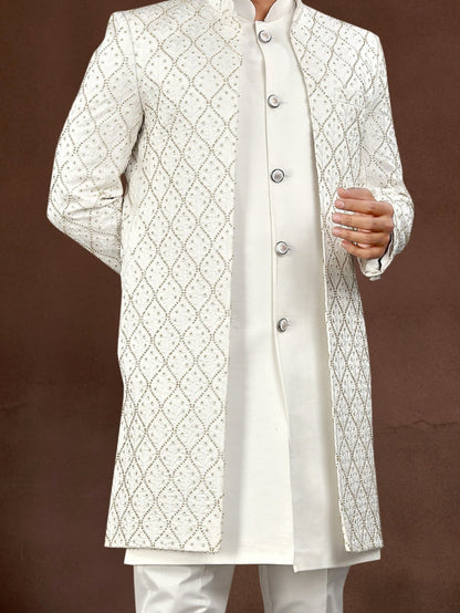 Man wearing a white sherwani with intricate patterns against a brown background