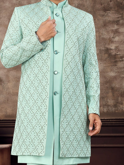 Man wearing a light green sherwani with a textured brown wall background