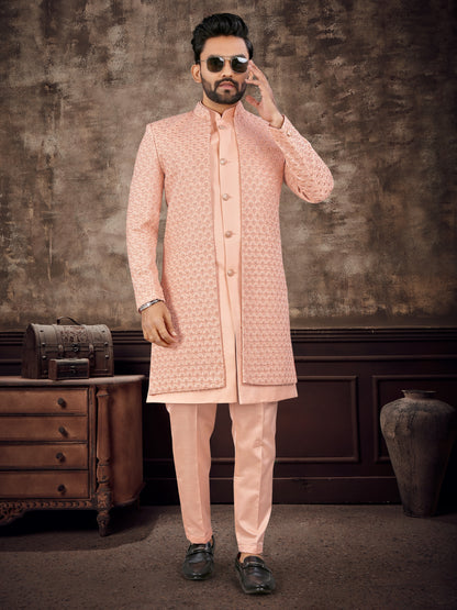 Man wearing a pink sherwani with sunglasses against a textured wall.