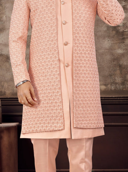 Man wearing a pink sherwani with sunglasses against a textured wall.